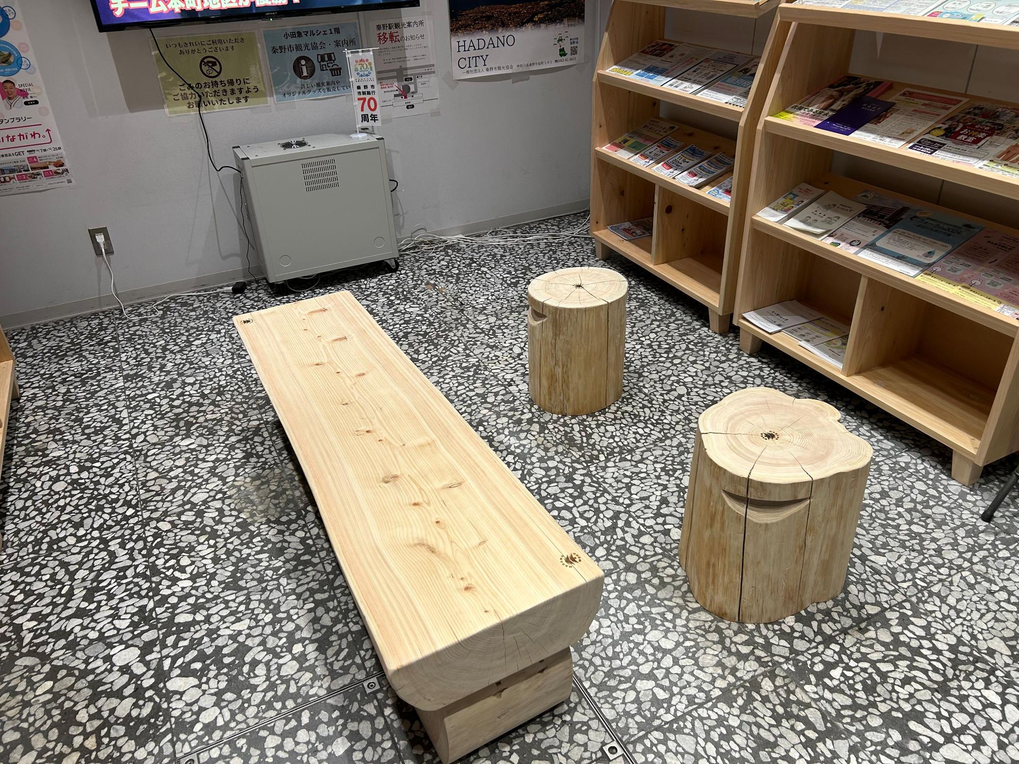 大きな木材の一枚板を使用した長いベンチと、切り株をそのまま利用した円柱形の椅子が2つ置かれた写真