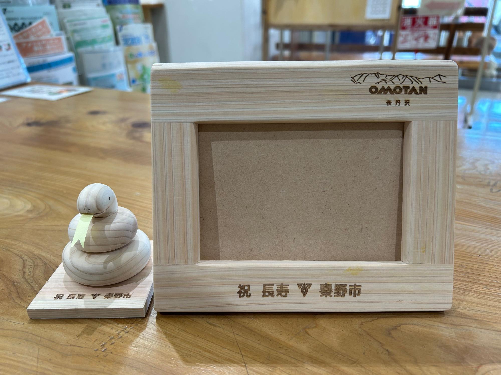 「OMOTAN 表丹沢」と刻印された木製フレームのフォトスタンドと、その左隣に置かれた舌を出した蛇をモチーフにした小さな木製置物の両方が、木目のある台の上に並べられている写真