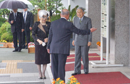雨が降る屋外で、天皇皇后両陛下が、出迎えるスーツ姿の男性と挨拶を交わしている写真