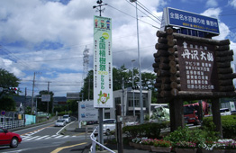 交差点付近で、右側には丸太で縁取られた木製の案内板と、中央には「全国植樹祭」と書かれた緑色の縦長の看板が設置されている写真