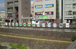 水無川沿いの石積みの護岸の上に、「全国植樹祭 平成22年5月23日」という文字が書かれたパネルが等間隔に並んで掲げられ、その奥には建物が立ち並ぶ街並みが見える写真