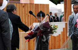 小学生くらいの子供が壇上でスーツ姿の男性から表彰を受け、花束を抱えている写真