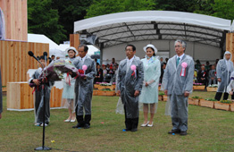 雨の野外式典で、胸に式典リボンを付けた男女数人がが立っている写真