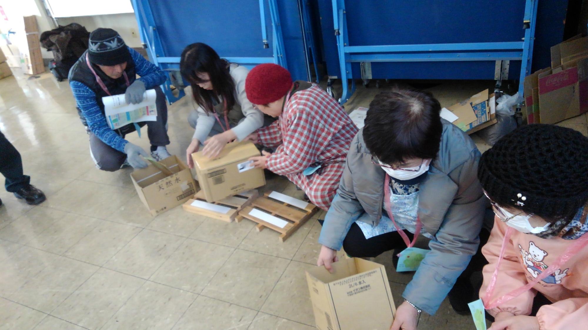 人々が床に座り、段ボール箱でダンボールコンポスト作成体験を行っている様子を撮影した写真