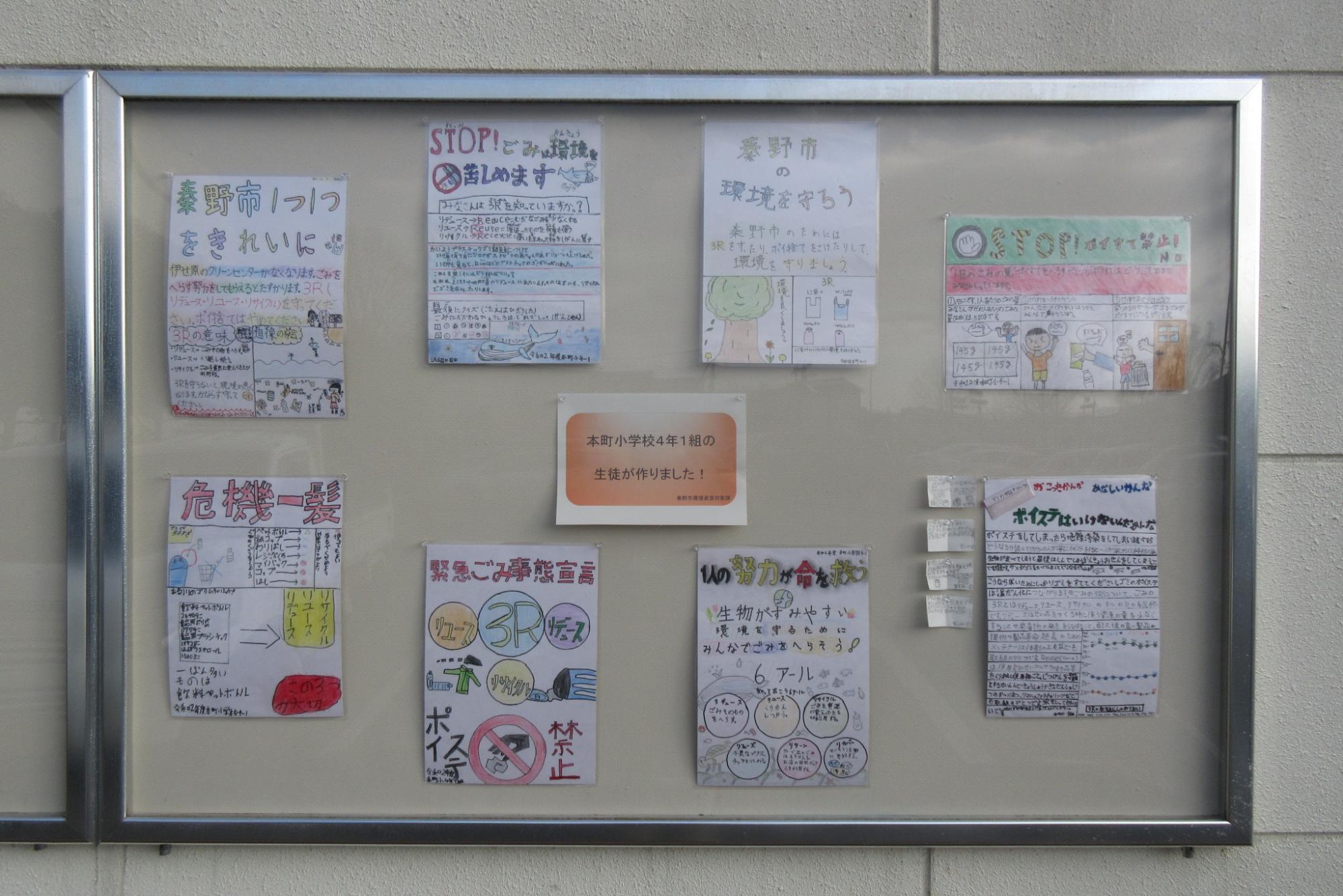 中央に「本町小学校4年1組の生徒が作りました」という張り紙が掲示された掲示板の中に、秦野市の環境やごみ問題に関する「秦野市の環境を守ろう」や「STOP！ポイ捨て禁止」など、児童たちが作成した8枚の啓発ポスターが展示されている写真