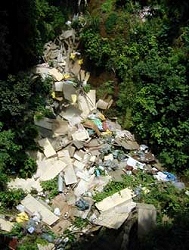 山の中の鬱蒼とした草木の中に、大きなコンクリート片や建築廃材、プラスチックごみなどが大量に投棄されている、堀山下の不法投棄現場を上から撮影した写真