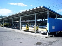 青い壁と屋根の車庫の下に、黄色いトラックが3台並んで停車している様子を撮影した写真