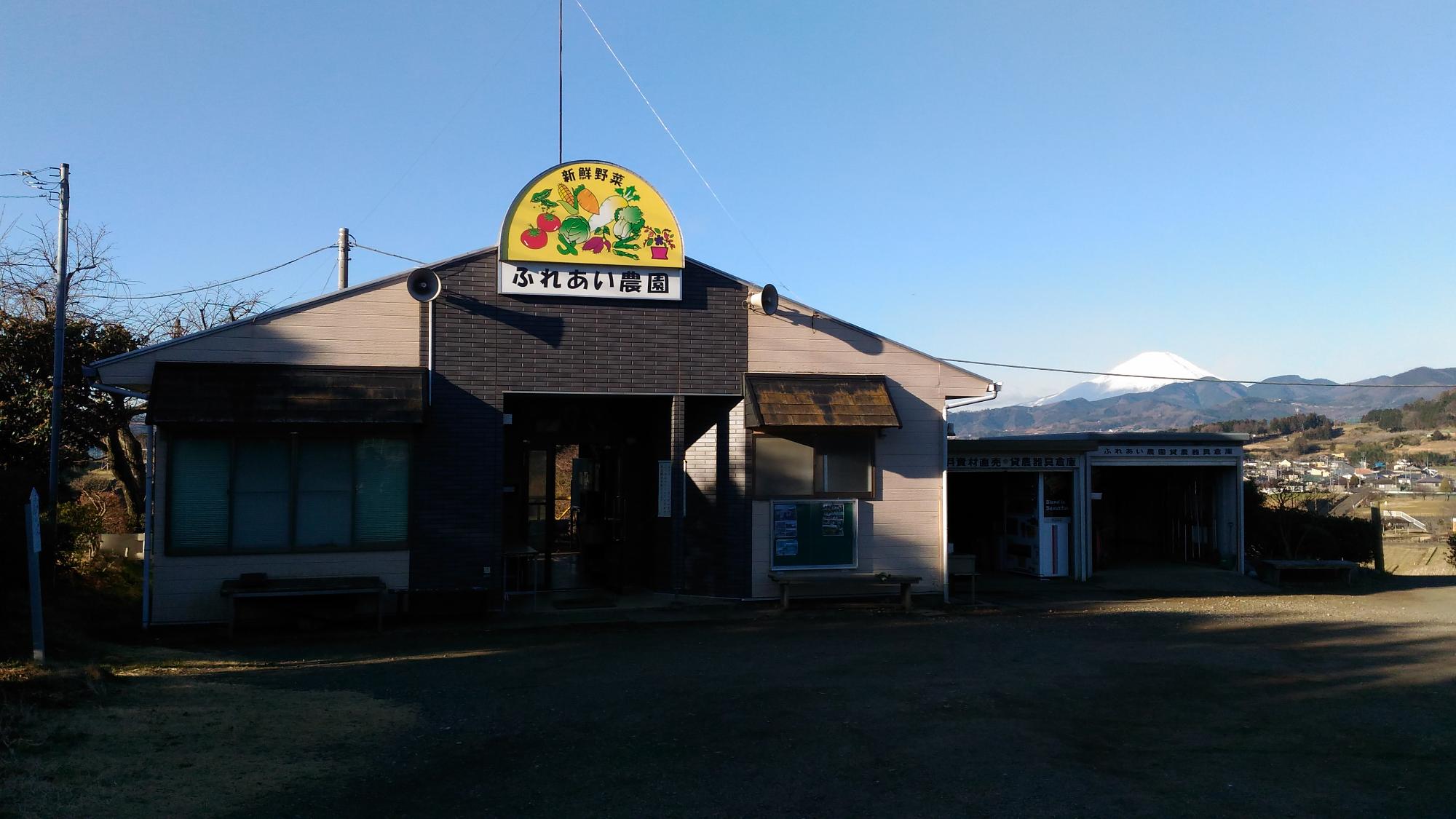 富士山の雪化粧を遠景に、「ふれあい農園」という看板を掲げた建物の外観写真