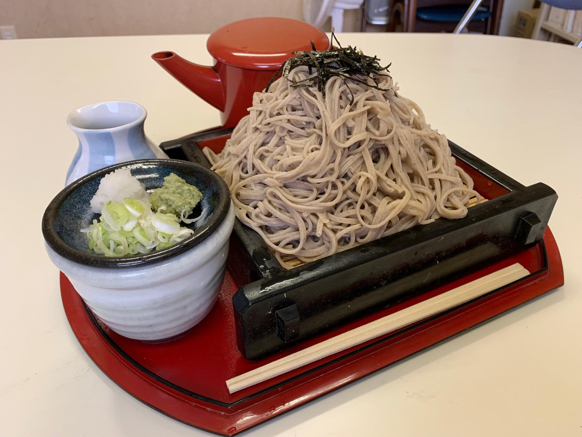 高く山盛りにされ上に刻み海苔がトッピングされた笊蕎麦と、薬味の大根おろし、刻みネギ、わさび、つゆが添えられた東雲山盛りそばの写真