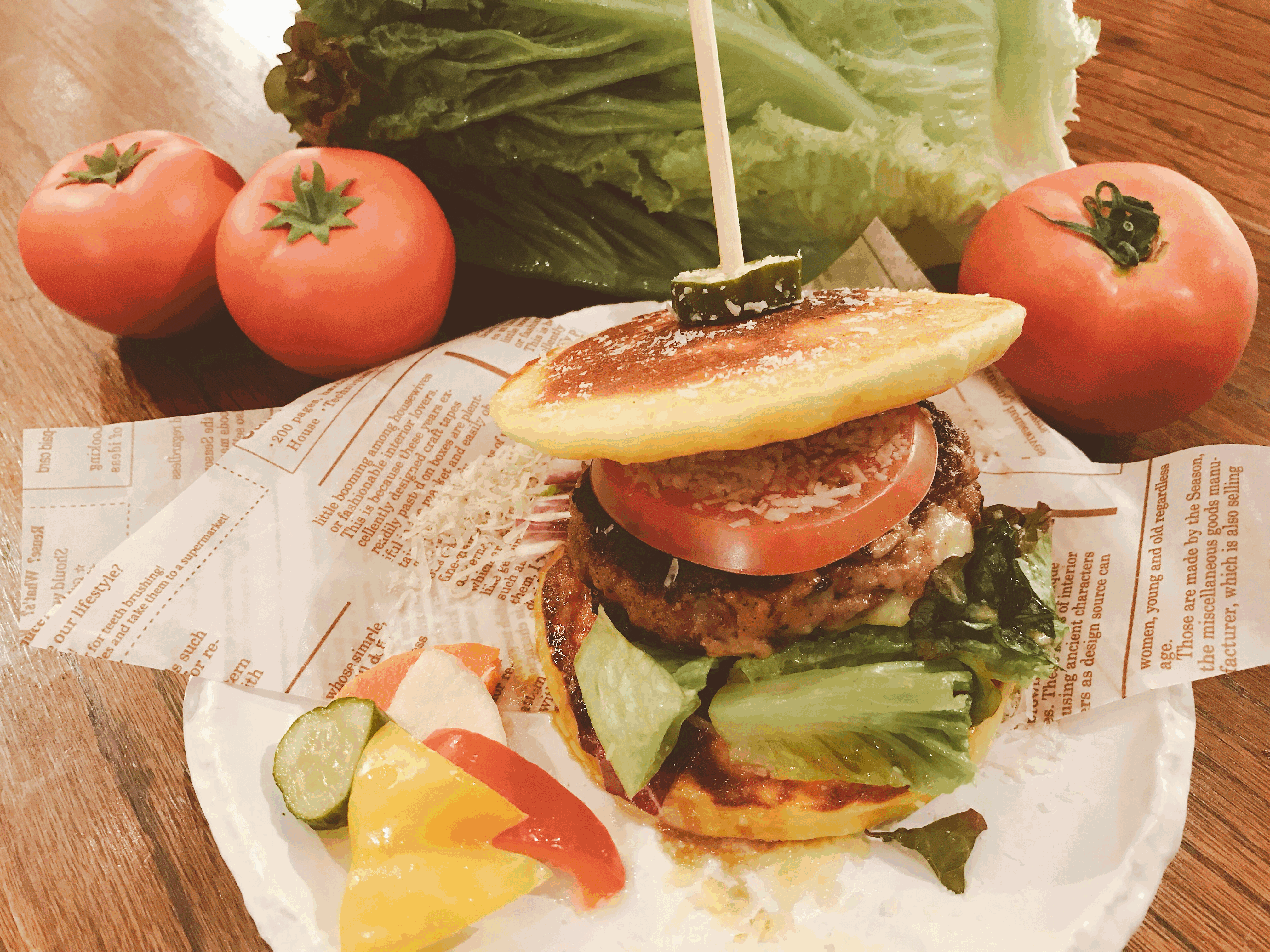 大きなバンズに厚いパティ、トマト、レタスを挟み、上部バンズのてっぺんにピクルスが串刺しにされている「丹沢チーズパンケーキバーガー」の写真