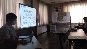 窓のある会議室で、マスクを着用した発表者がノートパソコンを操作し、「鳥獣被害対策と言ったら何を思い浮かべますか？」と書かれたスライドと地域の地図を映しながら説明している研修風景の写真