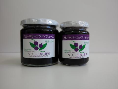ブルーベリーのイラストが描かれているラベルが貼られ、中に濃い紫色のブルーベリーコンフィチュールが入った透明の瓶が大小2つ並んで置かれている写真