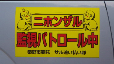 車体の灰色部分に貼られた黄色いマグネットステッカーで、赤い太文字で「ニホンザル監視パトロール中」と記され、その両脇に子ザルのイラストが描かれた看板