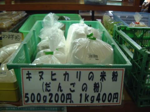 緑色のプラスチック製コンテナの中に、ビニール袋に小分けされた白い米粉が数多く入れられ、「キヌヒカリの米粉（だんごの粉）」と表示されている農産物直売所の写真