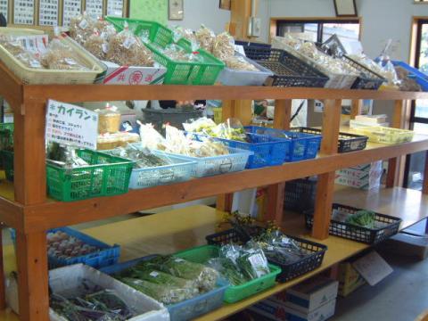 木製の棚に並べられたプラスチック製のカゴの中に、袋詰めされた様々な種類の乾燥食品や野菜が陳列されている農産物直売所の店内の写真