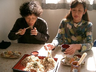 そば打ち体験の後、2人の女性が自分たちで打ったばかりのそばを、天ぷらと一緒に美味しそうに実食している様子の写真