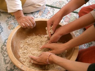 そば打ち体験で、床に置かれた大きな木鉢を数人で囲み、協力しながら粉に水を加えて生地をこねている手元の写真