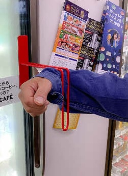赤非接触型の取っ手に腕を引っかけドアハンドルに触れずに開ける様子の写真