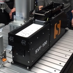 白い格子状の床面に設置された、黒い筐体に「SVF-I HD」と書かれた大型の産業用機器の写真