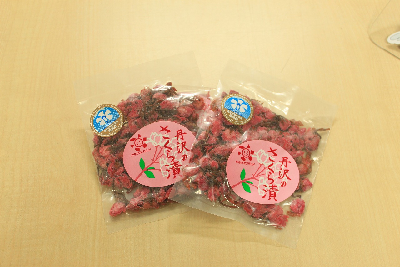 「丹沢のさくら漬け」と書かれたラベルが貼られ、透明なパッケージに詰められたさくら漬けが2つ並べて置かれている写真