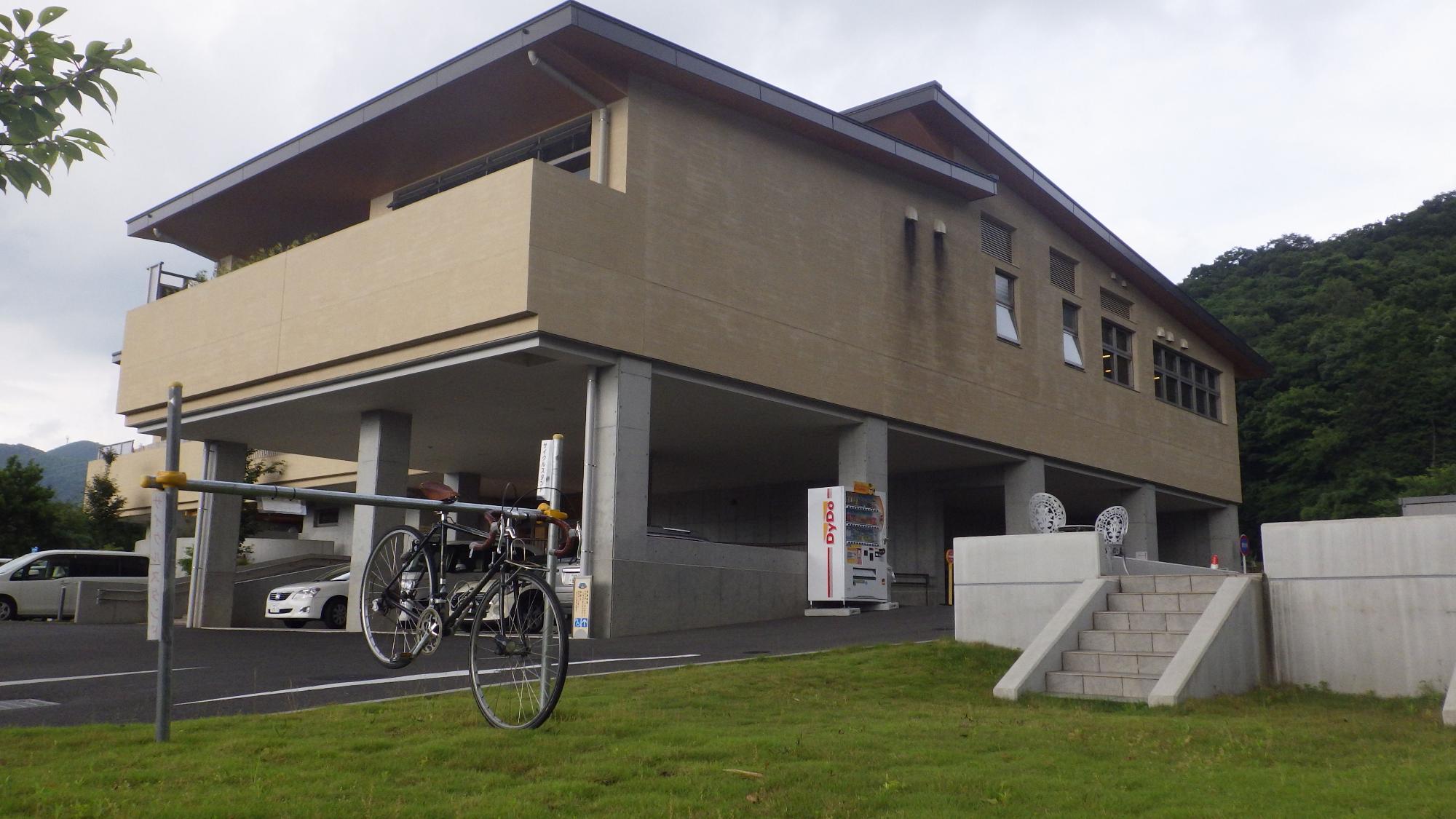 ピロティ構造の駐車スペースがあるベージュ色の建物の前の芝生に、サイクリングスタンドが設置されている写真