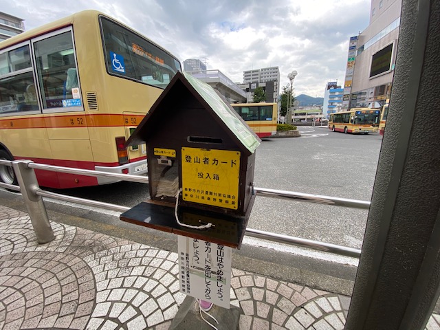 駅前やバス停と思われる場所に設置された家型の木製箱で、前面の黄色い板に「登山者カード投入箱」と記され、中には用紙が備え付けられている写真