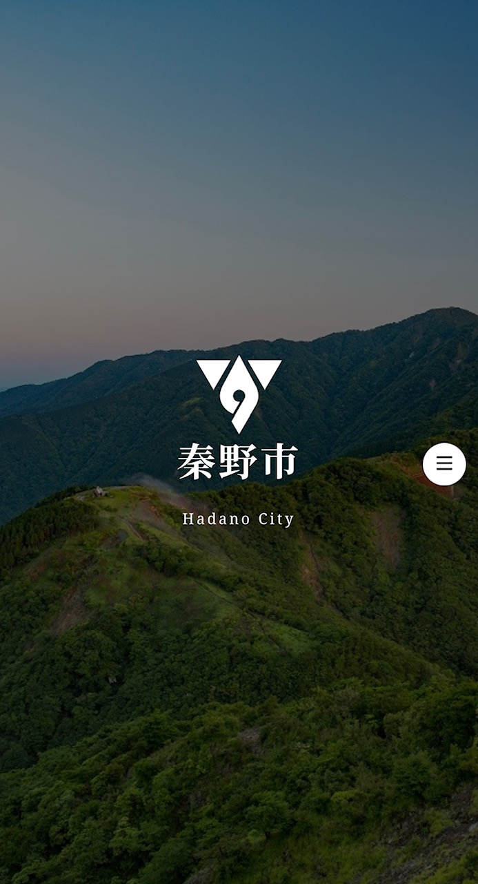 中央に灘の市の市章と「秦野市」の文字があり、背景に山脈が広がっているGuidoorのトップページ画像