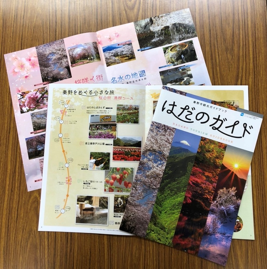 木のテーブルの上に、「はだのガイド」と書かれた表紙や、「桜の街 満喫コース」のページ、桜や名水を紹介するページなど、秦野市の観光パンフレットが複数枚広げられている写真