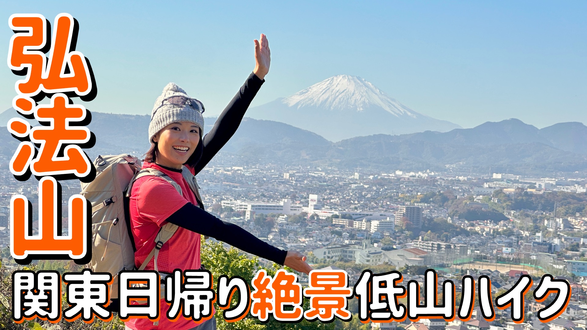 「弘法山」と「関東日帰り絶景低山ハイク」の文字があり、ニット帽を被った登山スタイルのかほさんが笑顔で手を挙げ、眼下に広がる街並みと、その奥に見える雪化粧した富士山を背景にポーズをとっている動画の一部画像