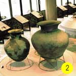 大小2つの緑がかった古代の壺が展示台の上に置かれている古墳展示館内部の写真に「2」と書かれた画像
