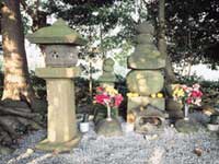 林の中にたたずむ、石灯籠や五輪塔の周りに花が供えられた源実朝公御首塚を写した写真