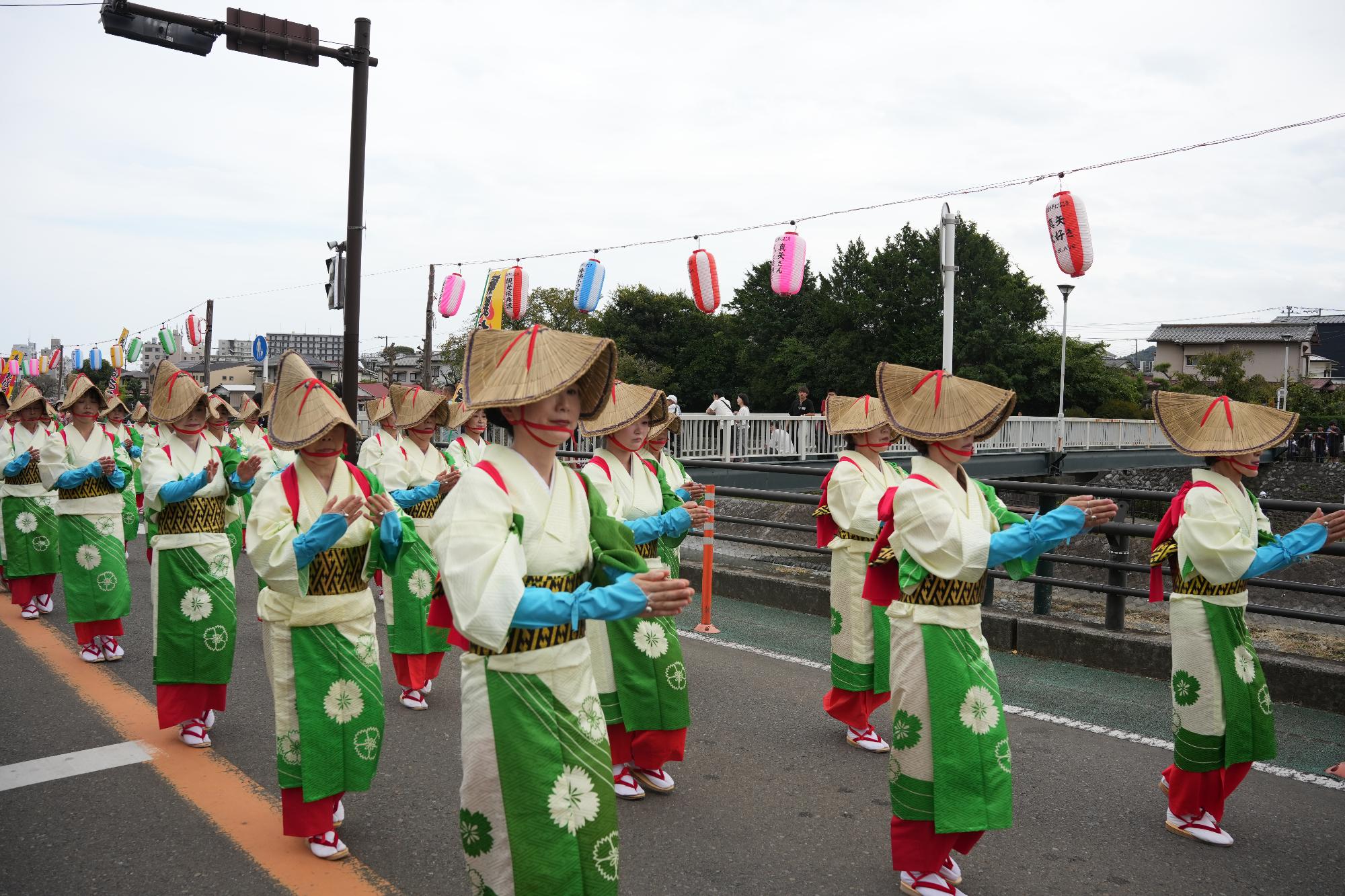 秦野たばこ祭のパレードで、お揃いの着物と編み笠を身にまとい、伝統的な踊りを披露しながら道を練り歩く女性たちの列。