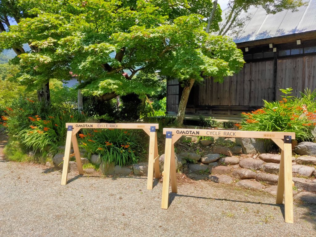 屋外に「OMOTAN CYCLE RACK」と描かれた木製のサイクルラックが2脚設置されている写真