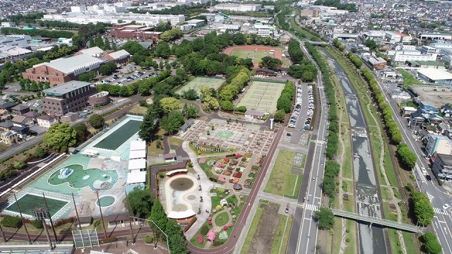 中央にはテニスコート、プール、広場、そして色とりどりの花が咲く花壇や遊歩道などの施設が整備されたカルチャーパーク全体を高所から写した写真