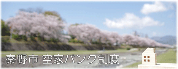 満開の桜並木と青空を背景に「秦野市 空家バンク制度」の白文字と小さな家の置物が配置された地域の空き家情報制度を紹介する広報用バナー