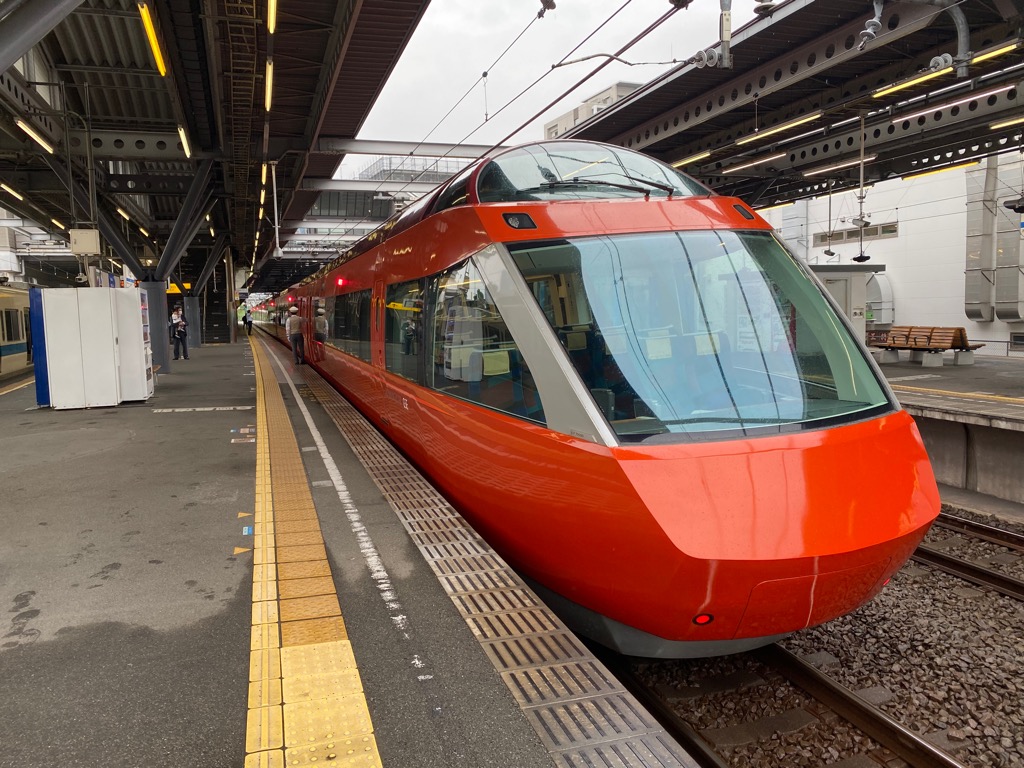 駅ホームに停車する鮮やかなオレンジ色のフロントガラスが大きく傾斜した流線型の列車の写真