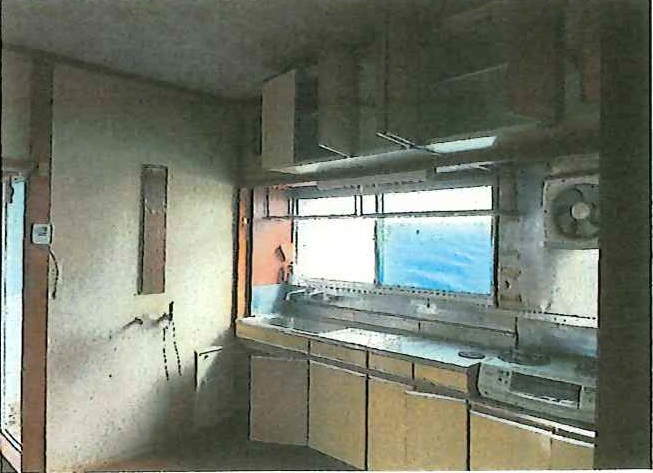 コンクリート打ちっぱなしの壁と天井の未完成キッチンスペースに、窓から青空が見え、シンクとキャビネットが設置途中の状態で撮影されたリフォーム前の写真