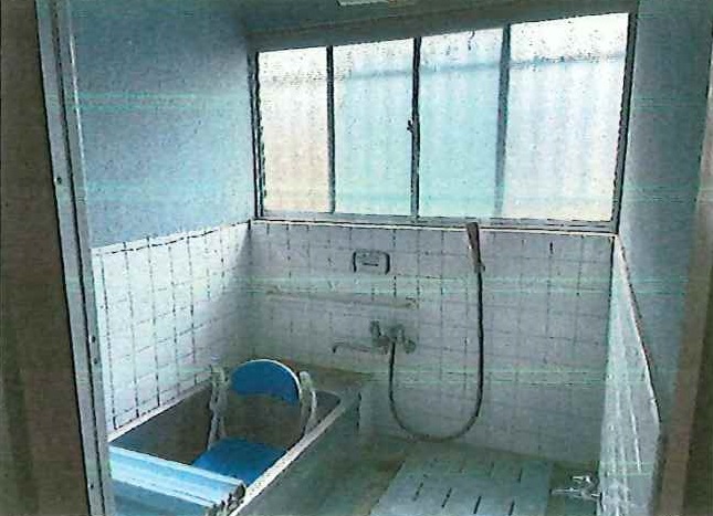 白いタイル壁と擦りガラス窓のある古い和式浴室に、青いプラスチック製バスチェアと洗面器が置かれ、老朽化が目立つリフォーム前の住宅浴室内部の写真