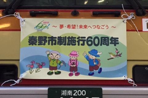 秦野市制施行60周年を記念し、「〜夢・希望！未来へつなごう〜」のスローガンの下に、登山帽をかぶった3人の子供と小鳥、花が描かれた横断幕を車両の後部に掲げた写真