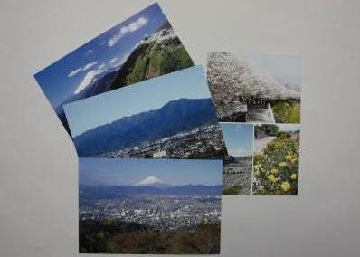 富士山と街並みを遠望する風景や山の稜線と麓の街、そして色とりどりの花畑の風景のポストカードが広げられている写真