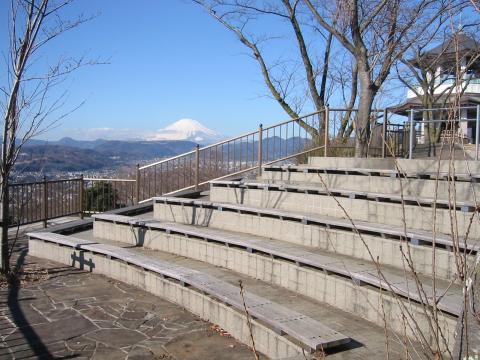 展望デッキの手すりの手前に、木製の座面が付いたコンクリートの階段状の席が設けられており、手すりの先には雪化粧の富士山を望む景色が見えている写真
