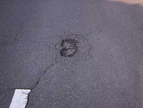 道路に縦横約15センチメートルほどの穴が開いており、その周囲にはひび割れが放射状に広がり、道路の損傷状態を写した写真