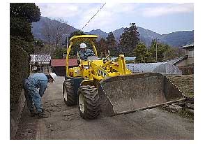 作業員が重機のショベルカーを使って道路の整備作業を行っている様子の写真