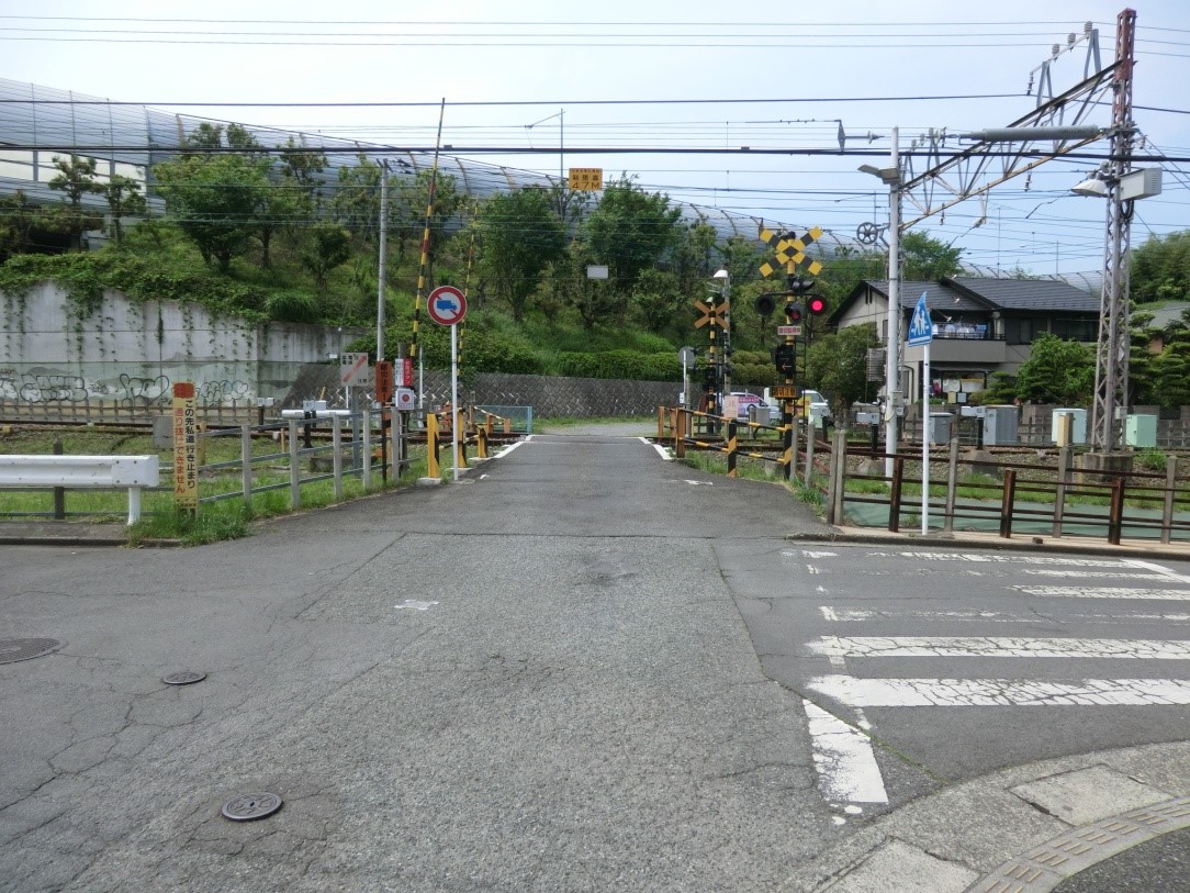 遮断機と警報機が設置された踏切の全景を交差点の道路から見た写真