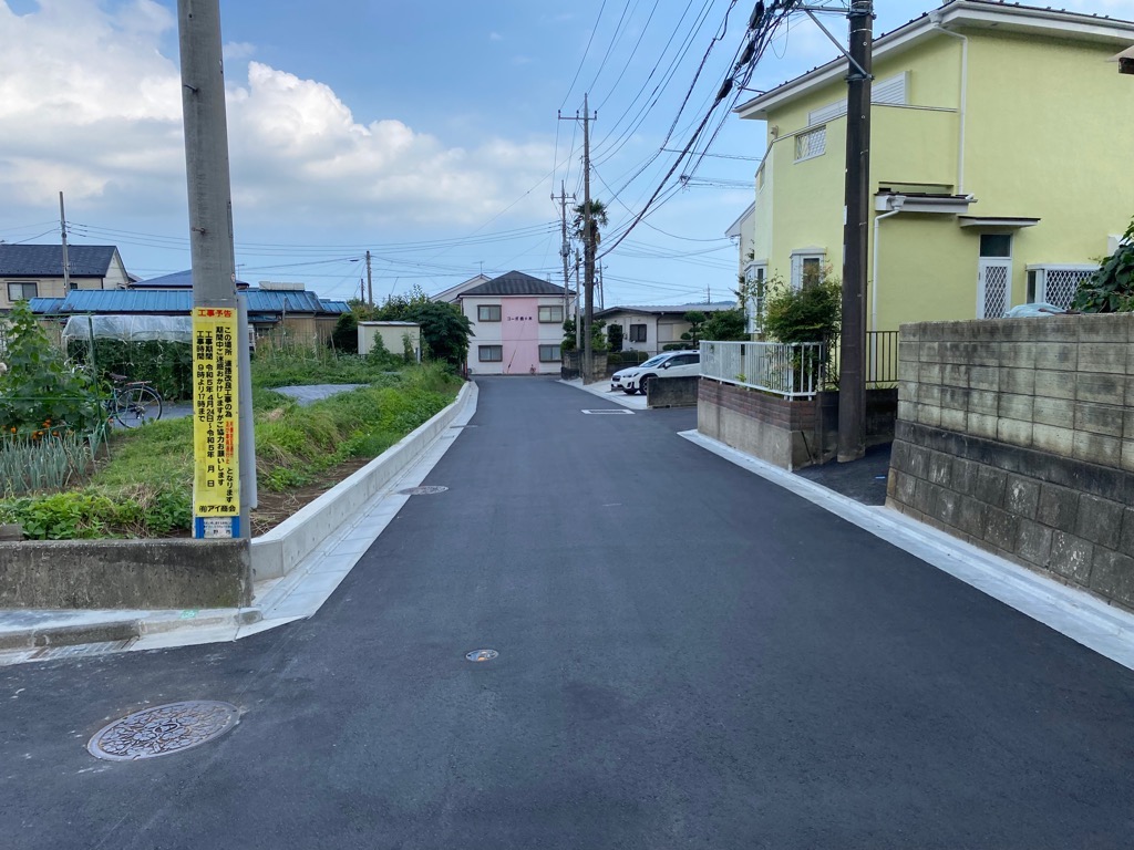 道路の左側の畑、右側の家の境目が整備され、新しく舗装された工事後の市道80号線の写真