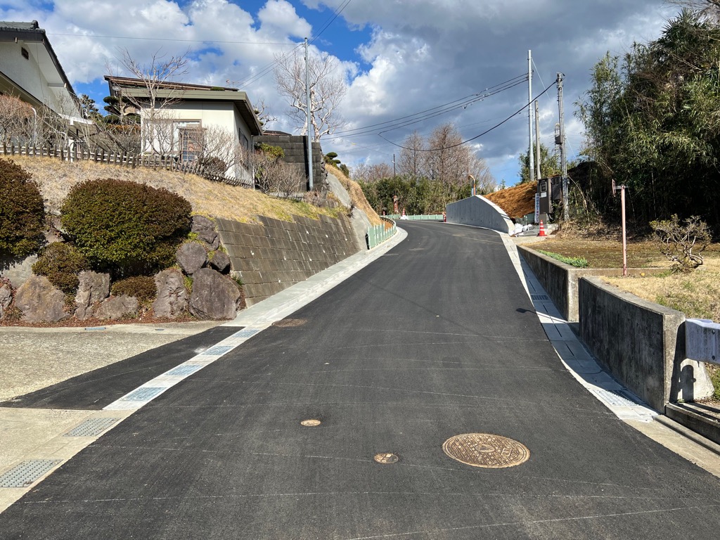 左側には住宅と石垣、右側にはコンクリートの擁壁と竹林があり、舗装が綺麗に整備された工事後の市道58号線の写真