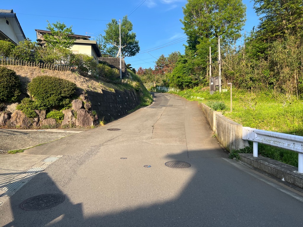 右側はガードレールと竹林、左側は石垣と住宅に挟まれた、工事前の市道58号線の写真