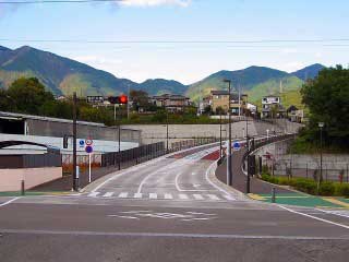 中央に三車線と横断歩道の白線が引かれた新しいアスファルトが舗装されている工事後の渋沢駅前の市道6号線の写真