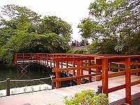 朱色で木造のウッドデッキが緑豊かな木々が生い茂る水面の上に架かっており、涼しげで落ち着いた雰囲気を醸し出す風景写真