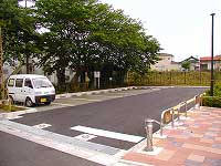 きれいに舗装された路面や周囲のブロックが整備され、白い軽バンが1台だけ停まっている木々に囲まれた公園の駐車場の写真